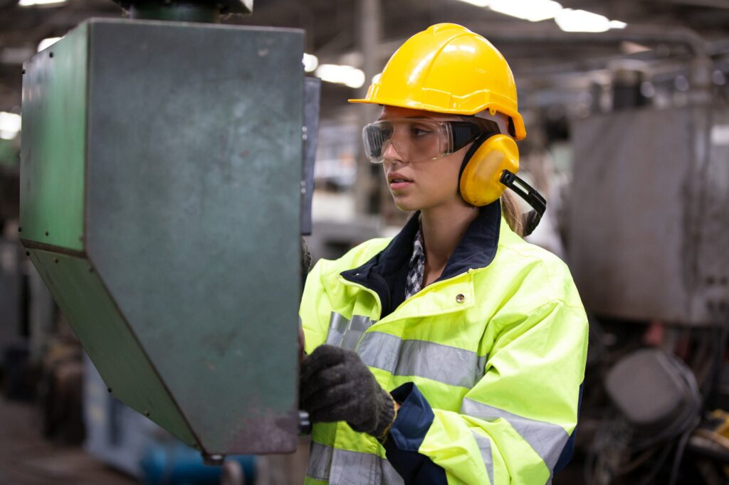 Woman worker wearing safety goggles control lathe machine to drill components. Metal lathe industria